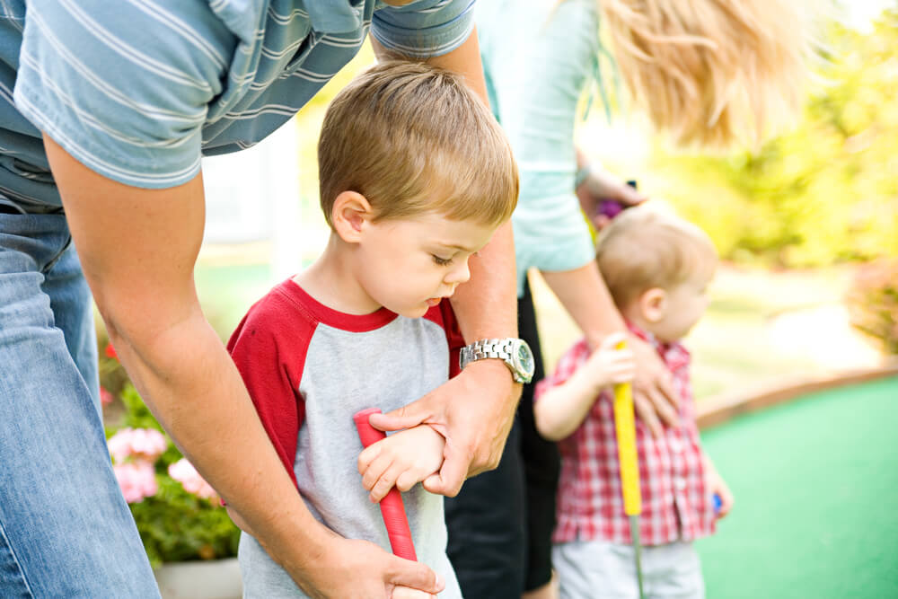 Parents playing mini golf with young boys.